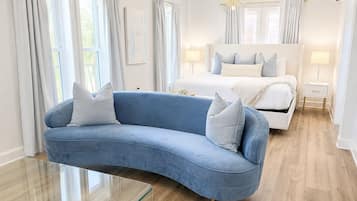 A modern bedroom with a curved blue sofa, a white bed, and a glass coffee table.