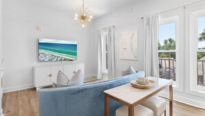 Ein modernes Wohnzimmer mit einem blauen Sofa, einem Esstisch, einem großen Fenster mit Vorhängen und einer Deckenleuchte.