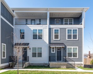 A two-story apartment building with a balcony on the upper floor, a front door, and a small front yard.