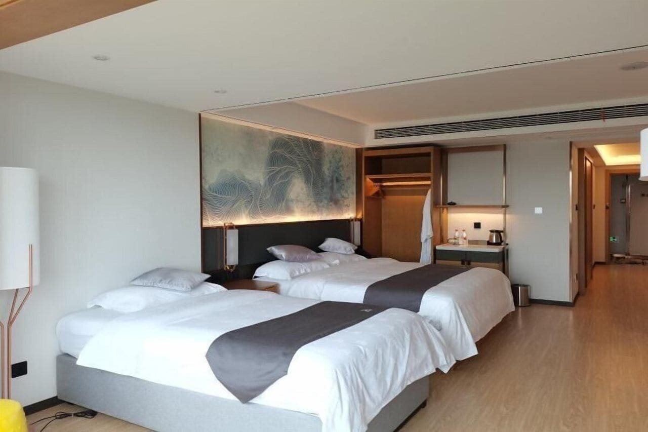 Hotellihuone, jossa on kaksi sänkyä, suuri taideteos seinällä, peili ja pieni työpöytä, jossa on lamppu.