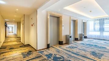 A hotel corridor with a patterned carpet, recessed lighting, and doors leading to rooms.