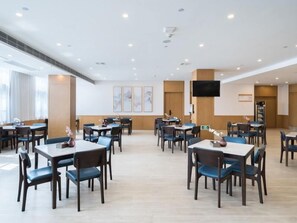 A hotel dining area with multiple tables and chairs, a flat-screen TV mounted on the wall, and artwork on the walls. - Greentree Eastern Xuzhou High Speed Railway Station Square Yindi Automobile Market Hotel (Xuzhou)