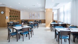 A spacious dining area with multiple tables and chairs, a wooden wall with shelves, and a large window providing natural light. - Greentree Eastern Xuzhou High Speed Railway Station Square Yindi Automobile Market Hotel (Xuzhou)