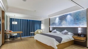 A modern hotel room with a large bed, a desk, a chair, and a wall-mounted artwork. - Greentree Eastern Xuzhou High Speed Railway Station Square Yindi Automobile Market Hotel (Xuzhou)