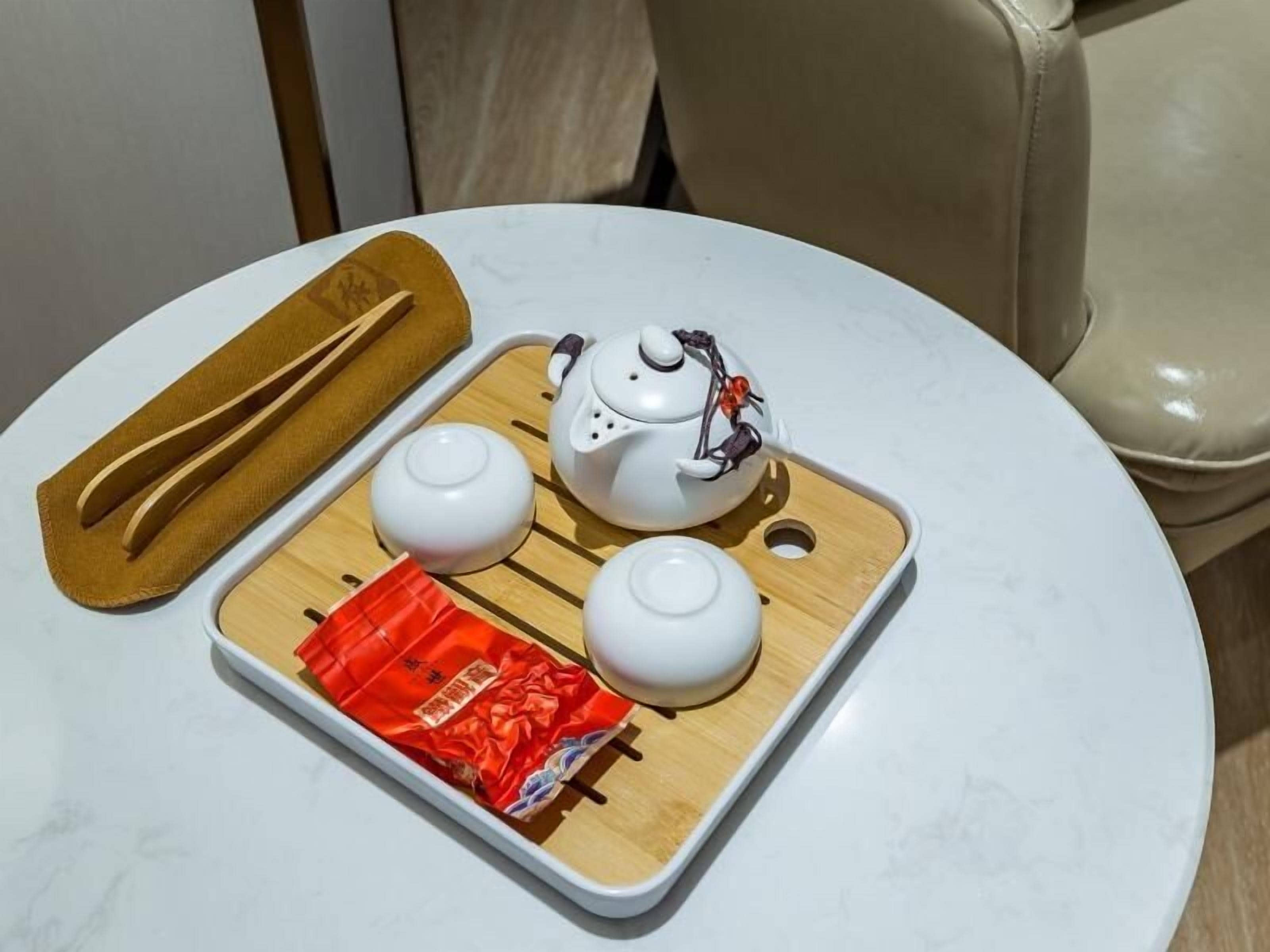 A white table with a tray holding a teapot, two cups, and a pair of chopsticks.