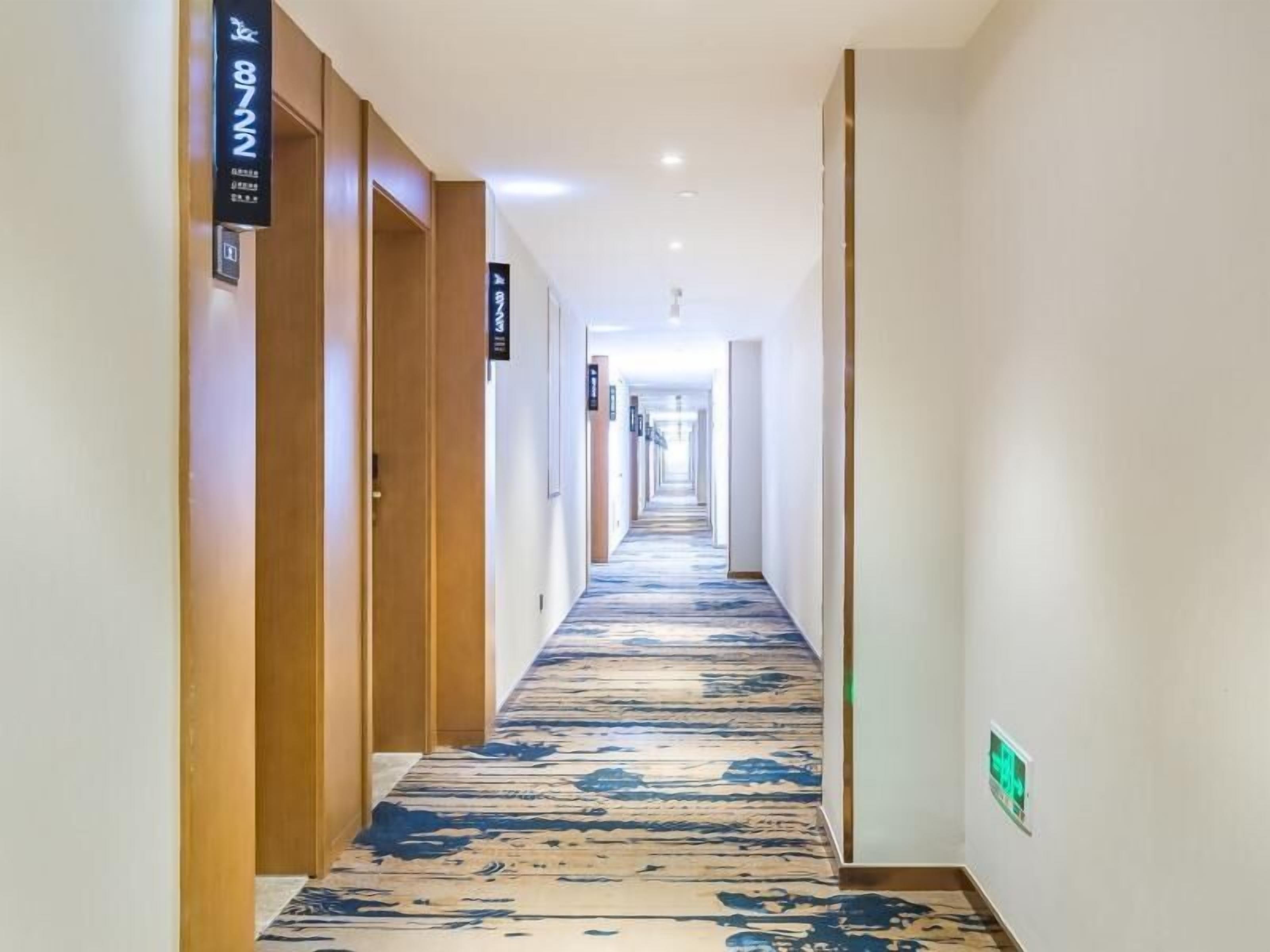 A hotel corridor with wooden doors, a patterned carpet, and directional signs.
