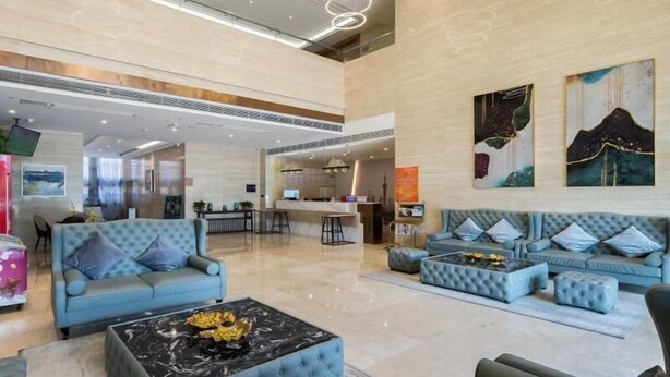 A spacious lobby with a high ceiling, a central seating area with sofas and ottomans, a marble coffee table, and artwork on the walls. - Greentree Eastern Xuzhou High Speed Railway Station Square Yindi Automobile Market Hotel (Xuzhou)