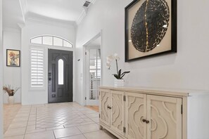 A hallway with a light-colored tiled floor, a cream-colored cabinet with decorative handles, and a framed artwork on the wall.