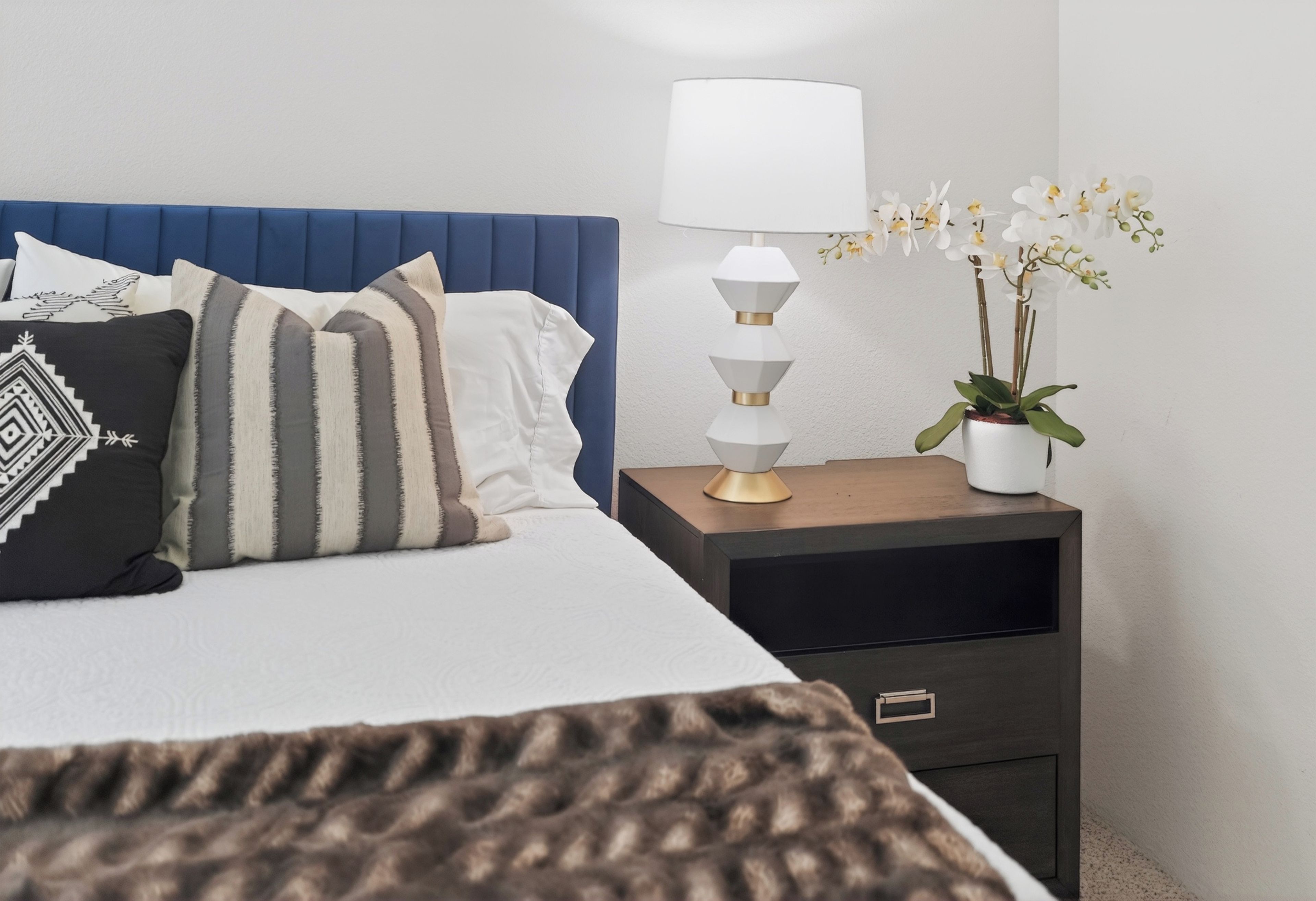 A neatly made bed with pillows, a bedside lamp, and a small potted plant on a nightstand.