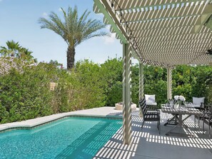 A poolside area with a pergola, lounge chairs, and a table set for dining.