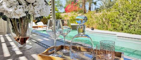 A tray with a decanter, glasses, and a vase of flowers by a poolside.