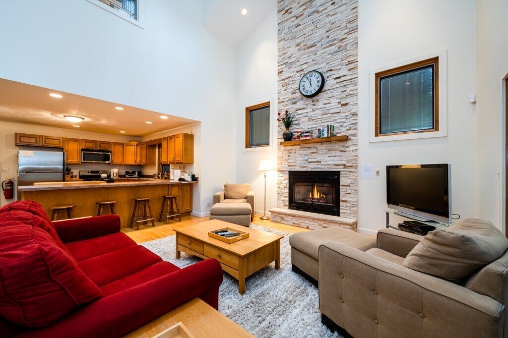 A spacious living area with a fireplace, a kitchen in the background, and a red sofa.