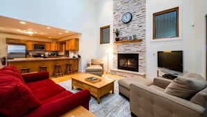 A spacious living area with a fireplace, a kitchen in the background, and a red sofa. - 2027 OPEN! (3 Nt Min) Harbert Home With Private Hot Tub Steps To Beach! (Harbert)