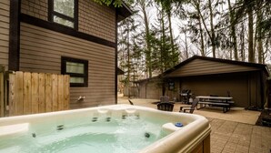 A hot tub in a backyard with a wooden fence, a barbecue area, and a covered patio. - 2027 OPEN! (3 Nt Min) Harbert Home With Private Hot Tub Steps To Beach! (Harbert)