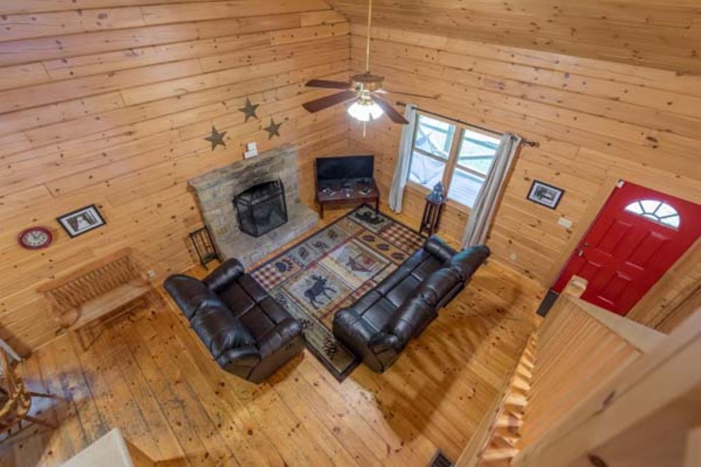 Interno di una baita di legno con camino, divano in pelle e ventilatore a soffitto.