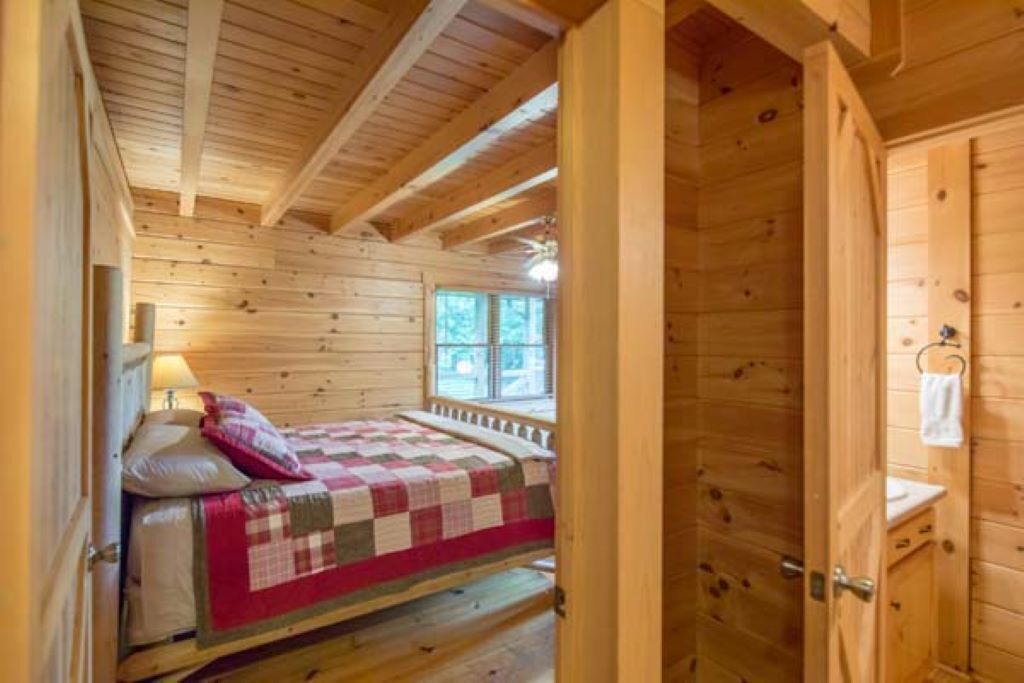 Ein Zimmer in einer Holzhütte mit einem Bett, einem Fenster und einem kleinen Badezimmer.