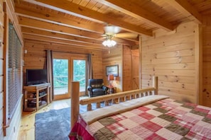 A log cabin bedroom with a bed, a television, and a chair.