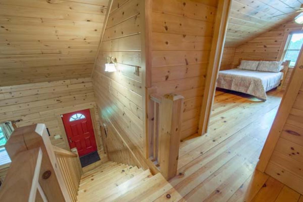 A wooden cabin with a staircase leading to a bedroom with a bed and a red door.