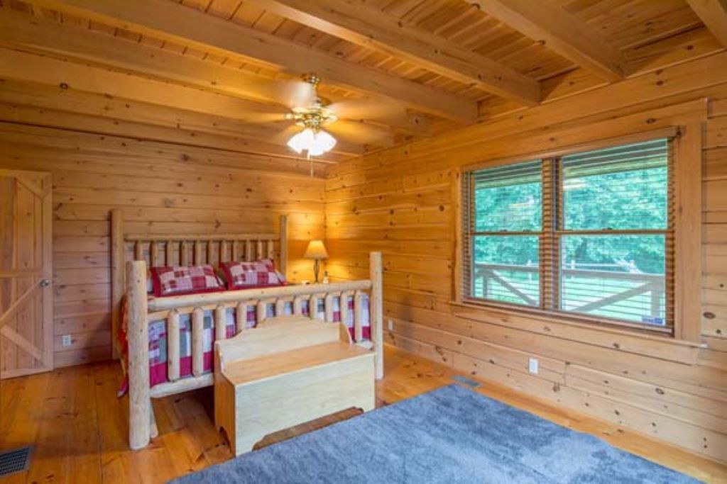 Um quarto de cabana de madeira com uma cama, uma janela e um ventilador de teto.