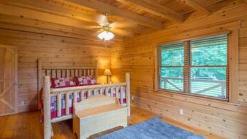 Um quarto de cabana de madeira com uma cama, uma janela e um ventilador de teto.