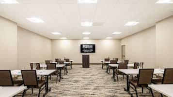 A conference room with tables and chairs, a carpeted floor, and a sign for Hilton Garden Inn.
