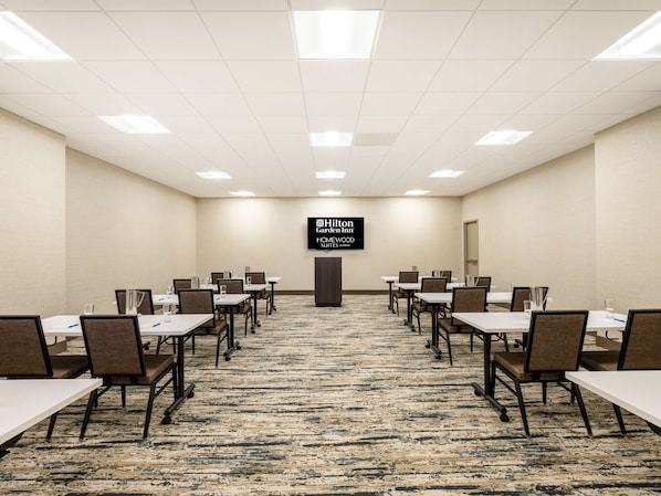 A conference room with tables and chairs, a carpeted floor, and a sign for Hilton Garden Inn.
