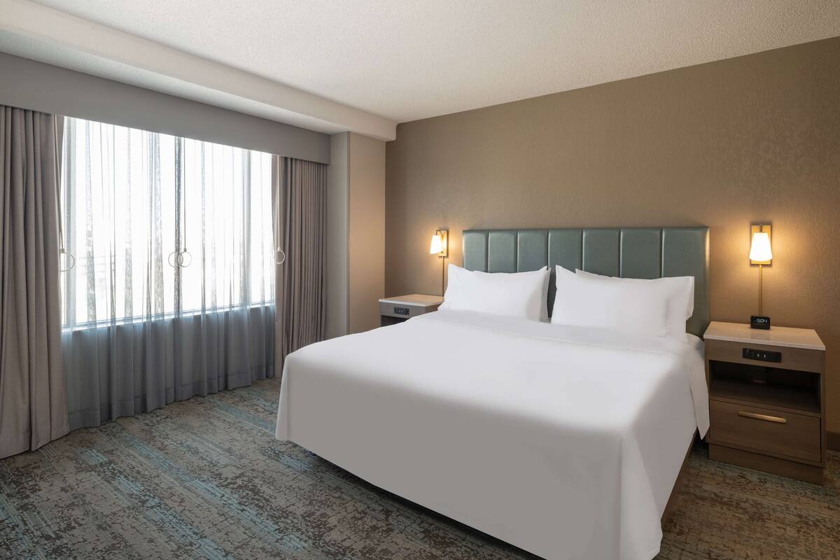 Een hotelkamer met een groot bed, twee nachtkastjes, een hoofdeinde en een raam met gordijnen.