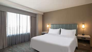 Habitación de hotel con una cama grande, dos mesitas de noche, cabecero y una ventana con cortinas.