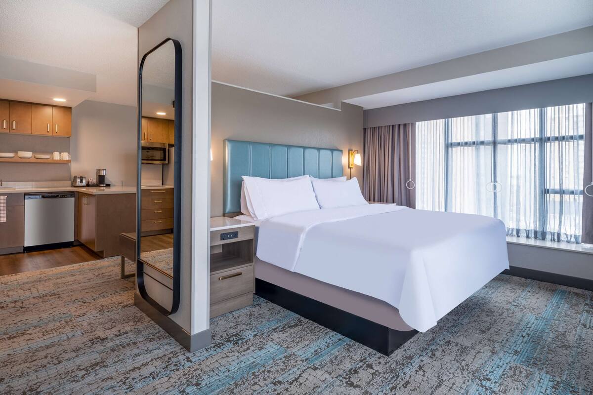 Een hotelkamer met een bed, een bureau, een kitchenette en een groot raam.