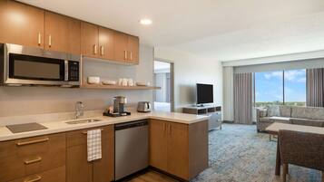 Quarto de hotel moderno com cozinha compacta, televisão de tela plana, sofá e área de refeições.