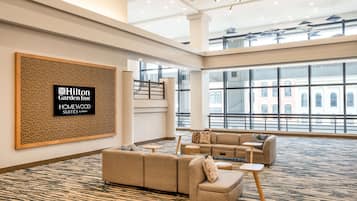 A spacious hotel lobby with a large seating area, a staircase, and large windows offering views of the city.