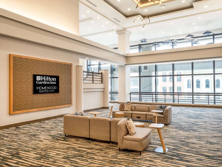 A spacious hotel lobby with a large seating area, a staircase, and large windows offering views of the city.