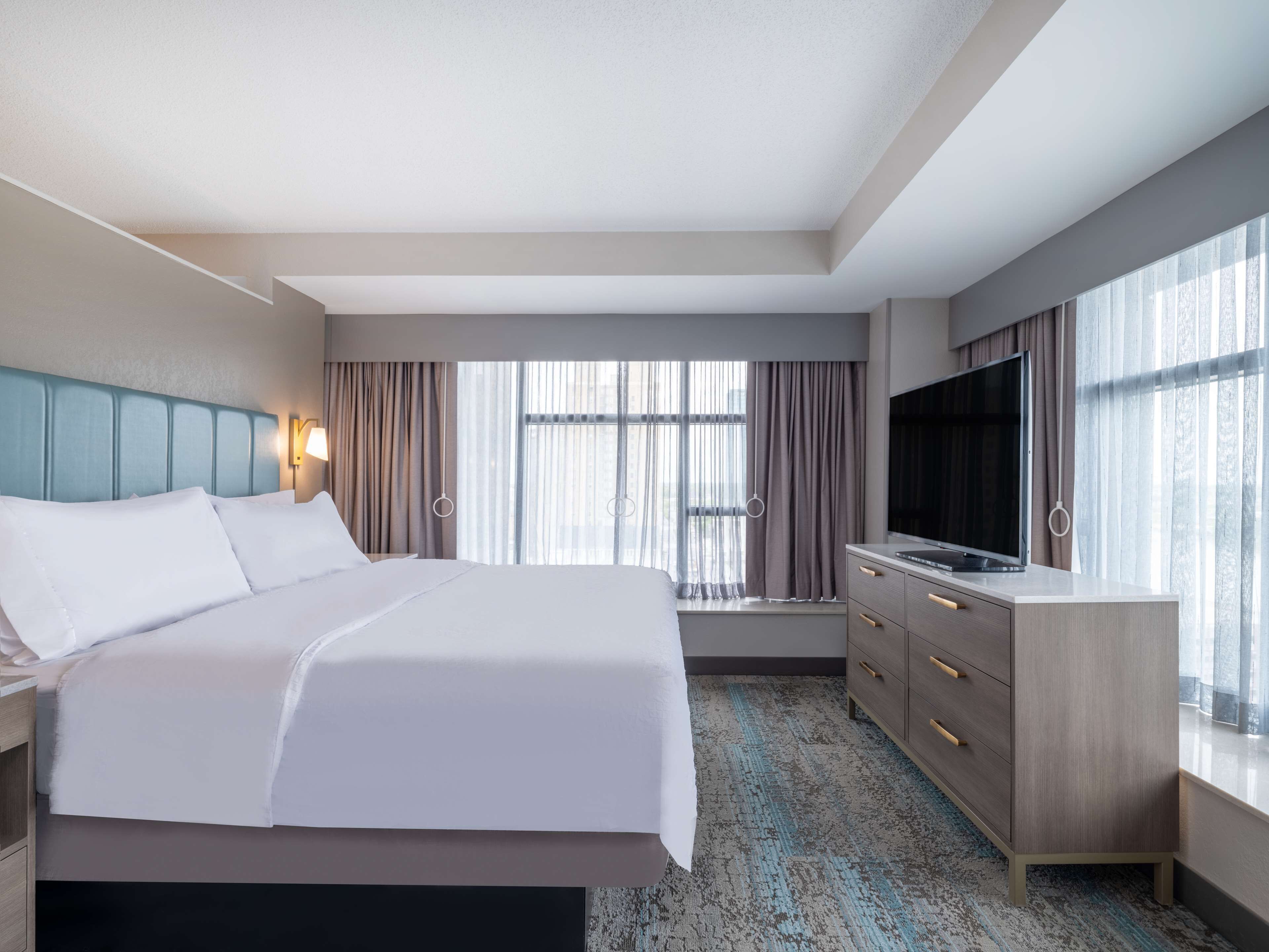 A hotel room with a large bed, a TV, a desk, and a window with curtains.