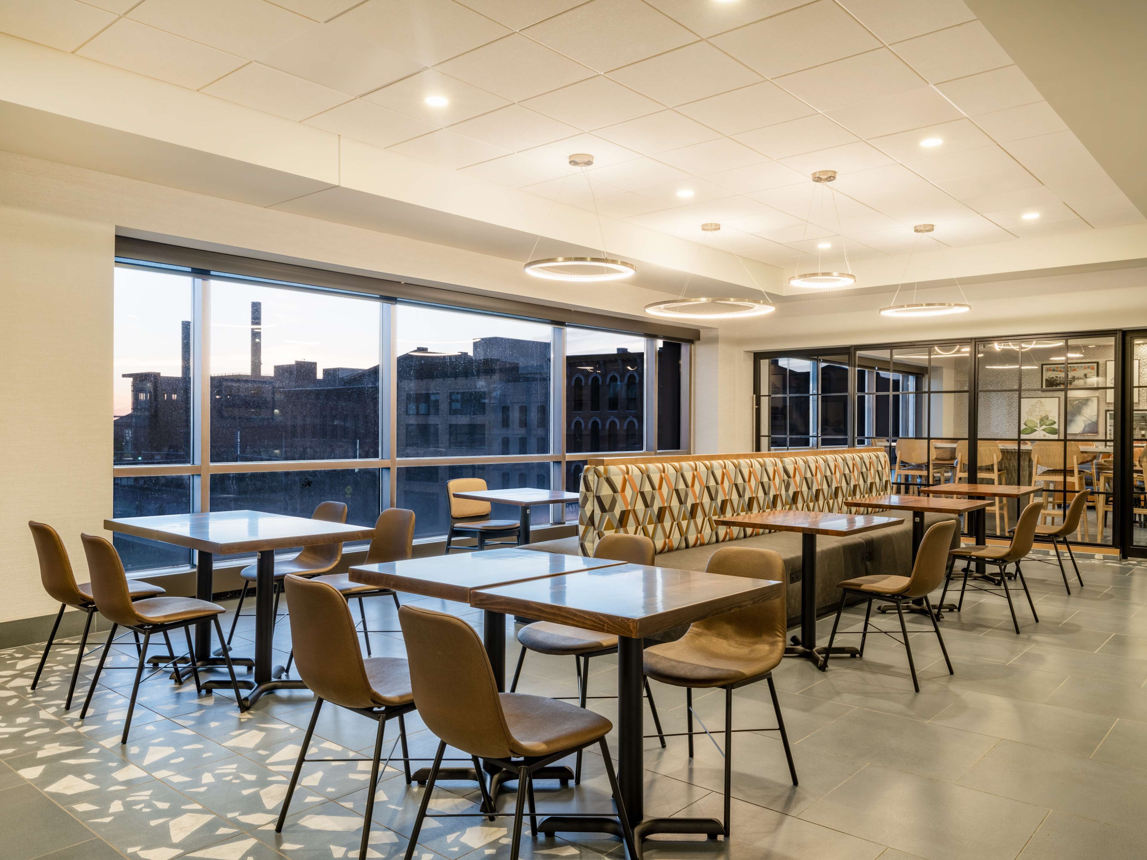 A modern dining area with high ceilings, large windows, and a view of the cityscape.