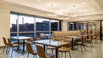 A modern dining area with high ceilings, large windows, and a view of the cityscape.