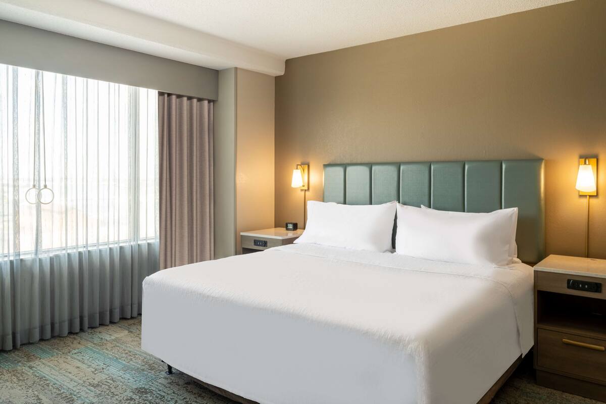 Een hotelkamer met een groot bed, twee nachtkastjes, een hoofdbord en een raam met gordijnen.