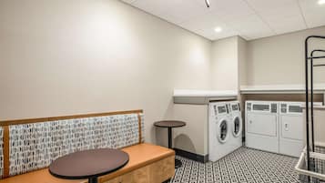 A laundry room with a bench, washing machines, and a small table.