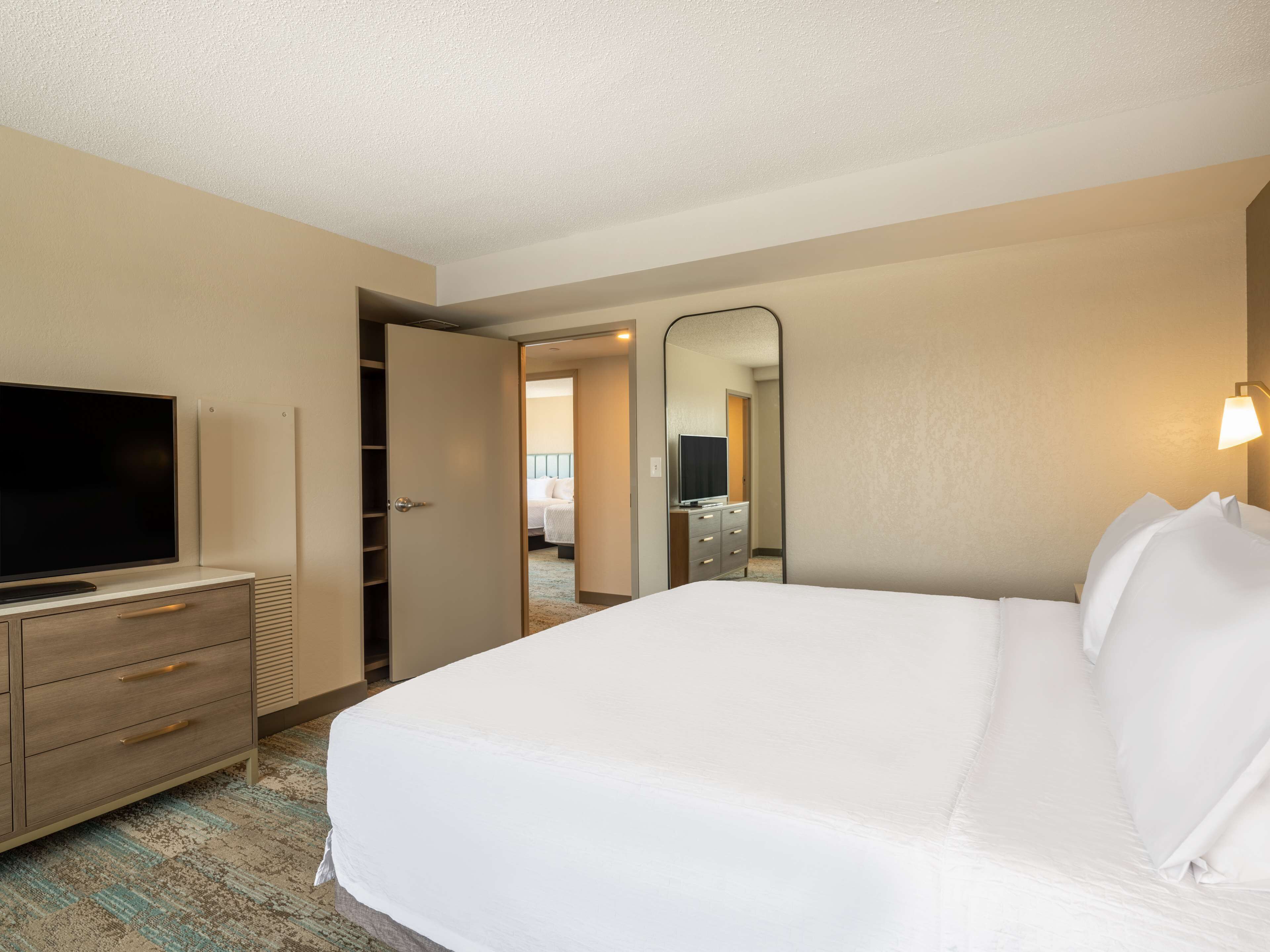 Una habitación de hotel con una cama, un televisor en una cómoda, un espejo y una cómoda con cajones.
