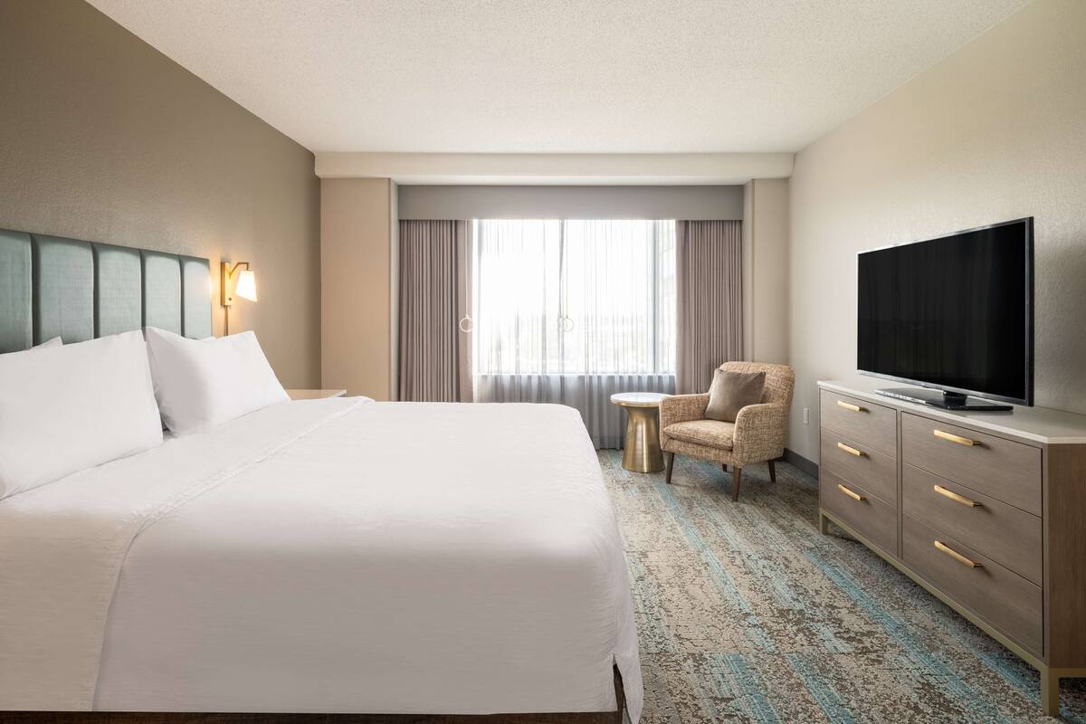 Een hotelkamer met een groot bed, een flatscreen televisie, een klein rond tafeltje, een stoel en een dressoir.