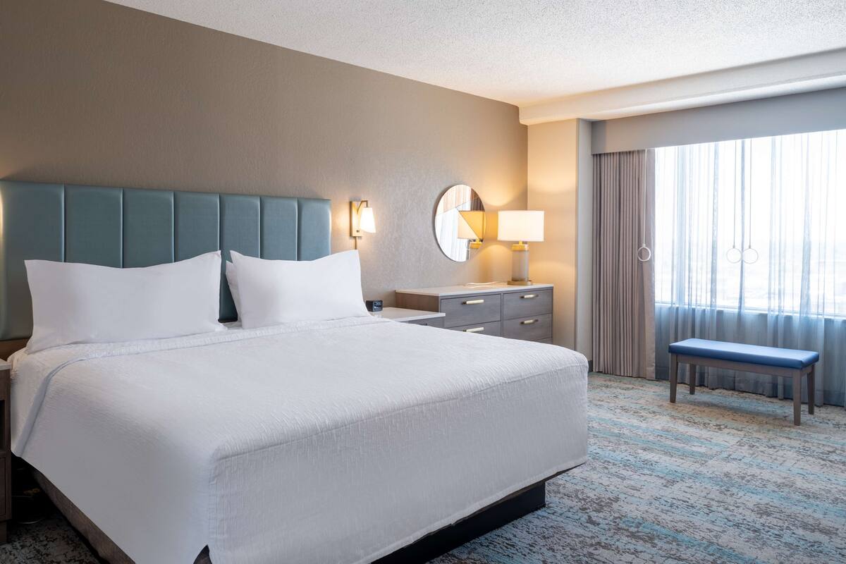 Een hotelkamer met een groot bed, een nachtkastje met een lamp, een spiegel en een bank.