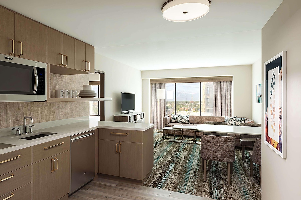 A compact hotel room with a kitchenette, a seating area with a view, and a large window.