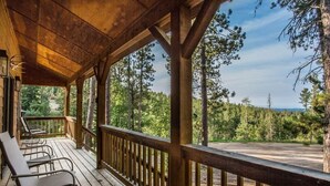 A wooden deck with chairs, a railing, and a view of a forested area.