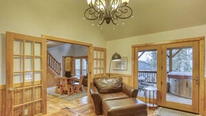 A spacious living room with a leather sofa, wooden flooring, a chandelier, and large sliding glass doors leading to an outdoor deck.