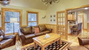 A cozy living room with a brown leather sofa, a wooden coffee table, and a chandelier.