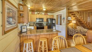 Una cocina con armarios de madera, una isla central con taburetes, un refrigerador y un microondas.
