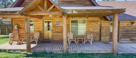 A log cabin with a porch, wooden deck, and two chairs.