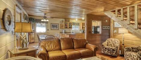L’intérieur chaleureux d’un chalet avec un plafond en bois, un canapé en cuir, des fauteuils à motifs, un coin repas et un escalier.