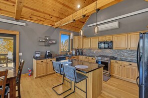A modern kitchen with wooden cabinets, a central island with bar stools, a built-in oven, and a large window providing a view of the outdoors. - Your Perfect Black Hills Adventure Starts at The Lodge on High Ridge Trail! (Lead)