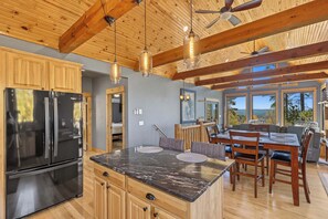 A spacious kitchen with a large island, wooden ceiling beams, and a view of the outdoors through large windows. - Your Perfect Black Hills Adventure Starts at The Lodge on High Ridge Trail! (Lead)
