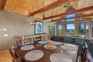 A spacious dining area with a wooden table and chairs, surrounded by large windows offering a view of the outdoors.